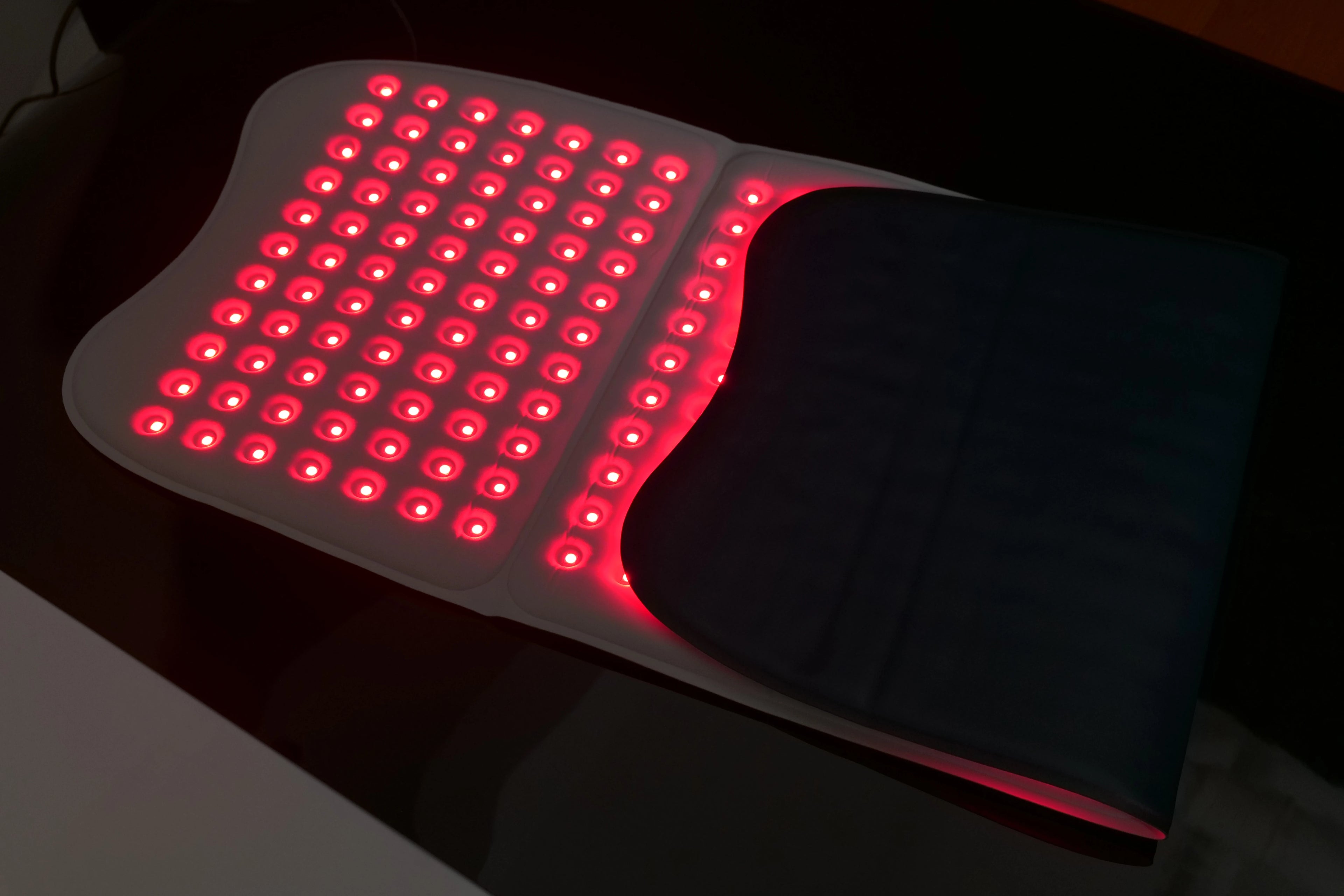 Large, rectangular red light therapy mat with many glowing red LED lights, partially folded on a dark surface.