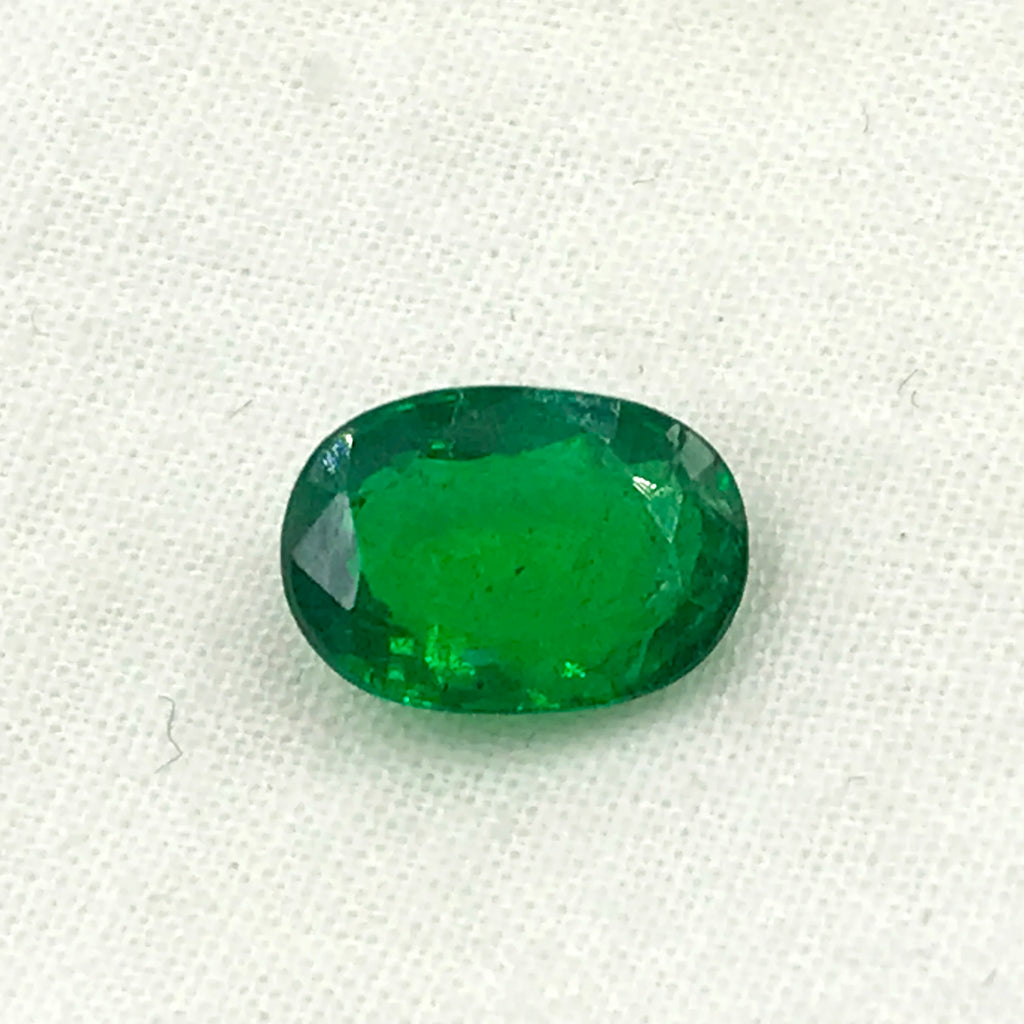 Green oval faceted loose gemstone with natural texture, centered view