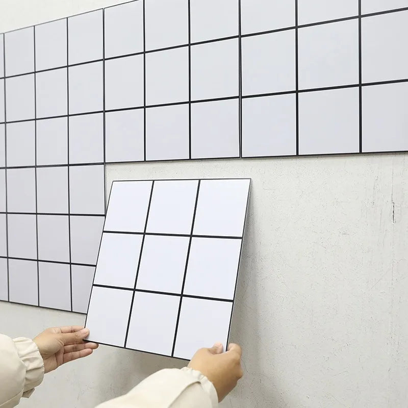 White square peel-and-stick tile sheet with black grid lines, held in hands