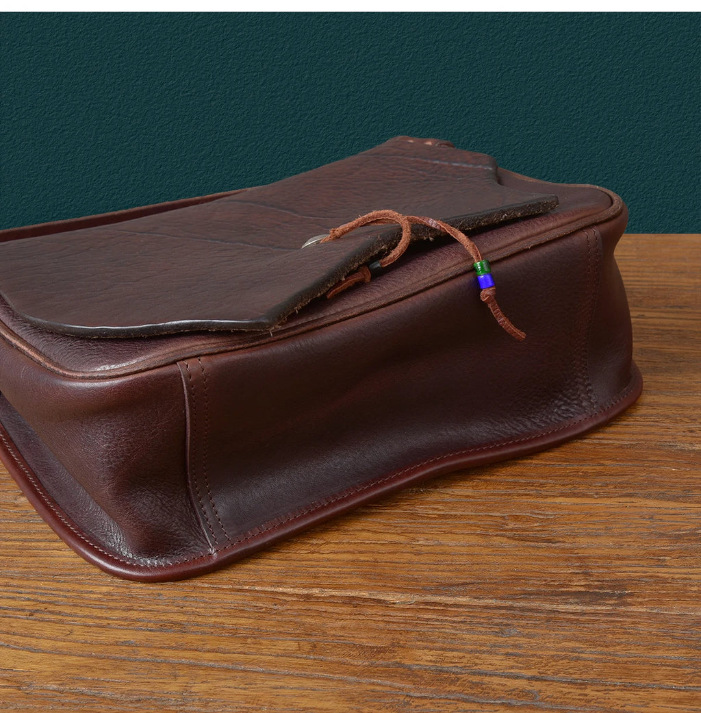 PNDME vintage dark brown cowhide leather messenger bag with handcrafted flap closure and decorative bead detail.