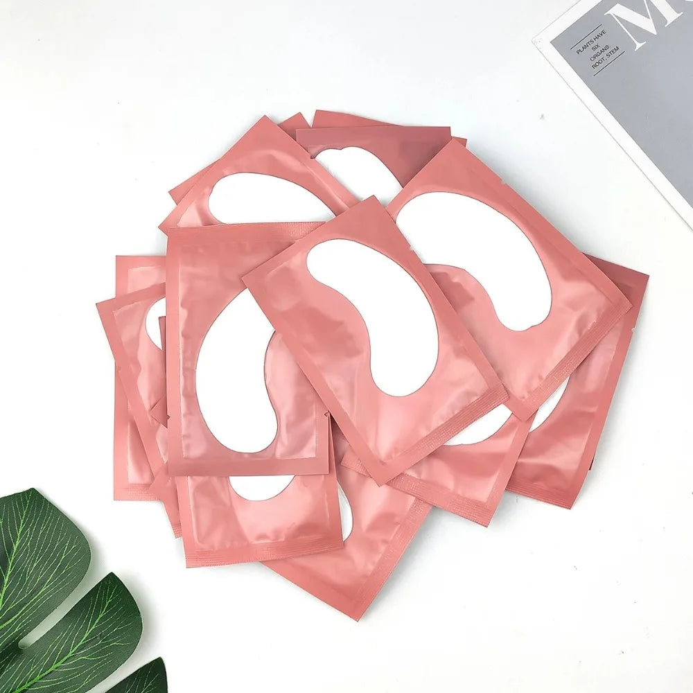 Pile of pink individual foil sachets containing white under-eye gel patches for eyelash extension application.