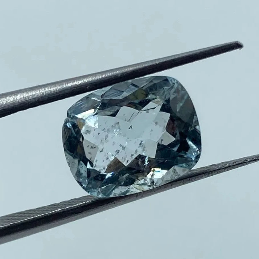 Loose cushion-cut aquamarine gemstone, sky blue, held between tweezers, close-up view