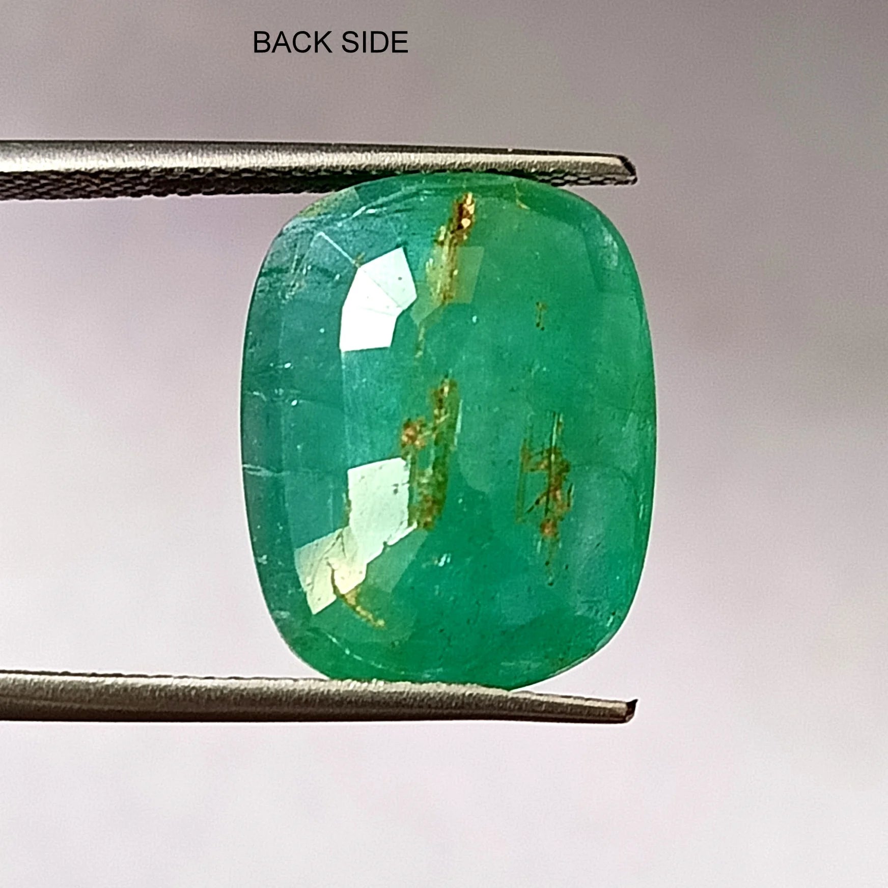 Green oval emerald gemstone back view, faceted, with visible gold-toned inclusions.