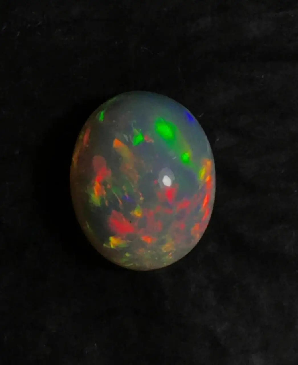 Oval opal cabochon with green, red, and blue flashes, glossy dome.