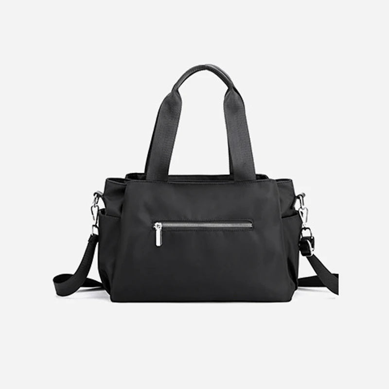 Minimalist black designer handbag, nylon satchel with top handles, zipper pocket, and adjustable shoulder strap.