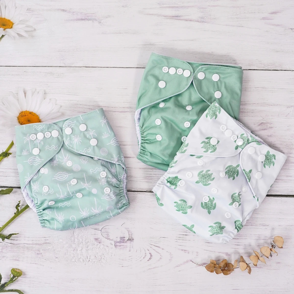 Three reusable cloth baby diapers in green sea turtle and palm tree prints on a white wood background.