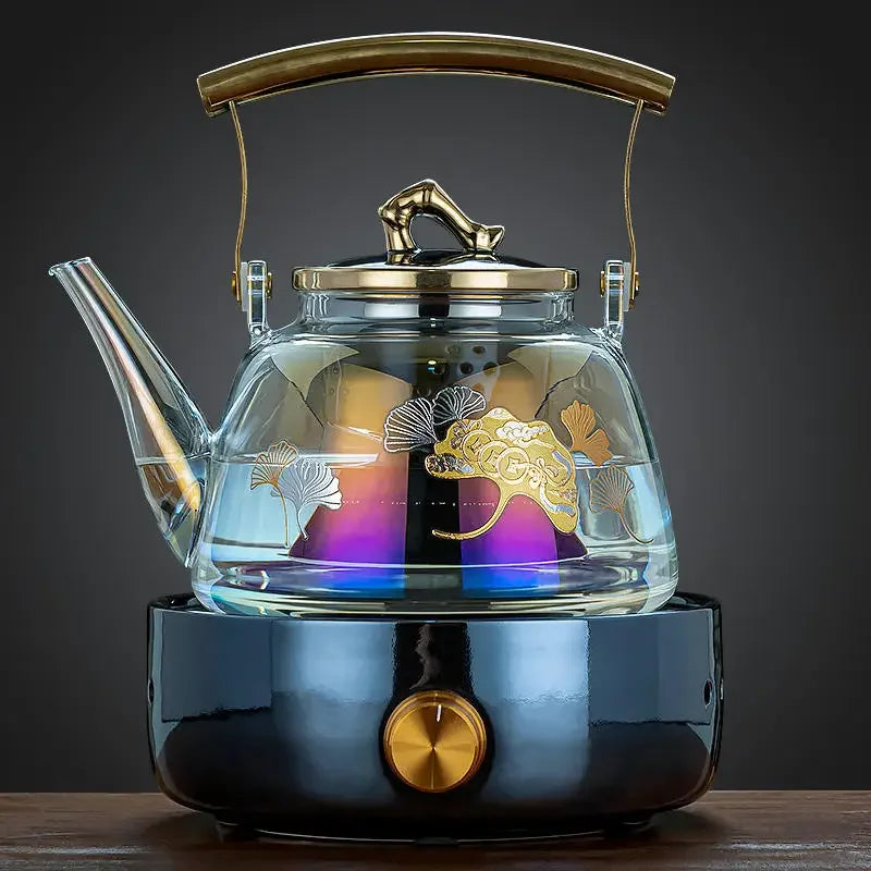 Elegant glass tea kettle with gold ginkgo leaf design, gold handle, and black electric stove base.
