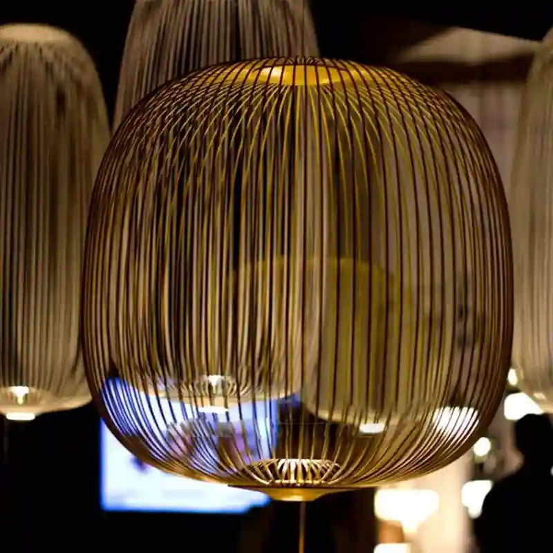 Large spherical pendant lamp made of vertical gold-toned metal wires, used for ambient indoor lighting.