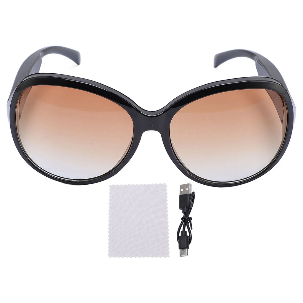Oversized black smart camera sunglasses with gradient brown lenses, a cleaning cloth, and a USB charging cable.