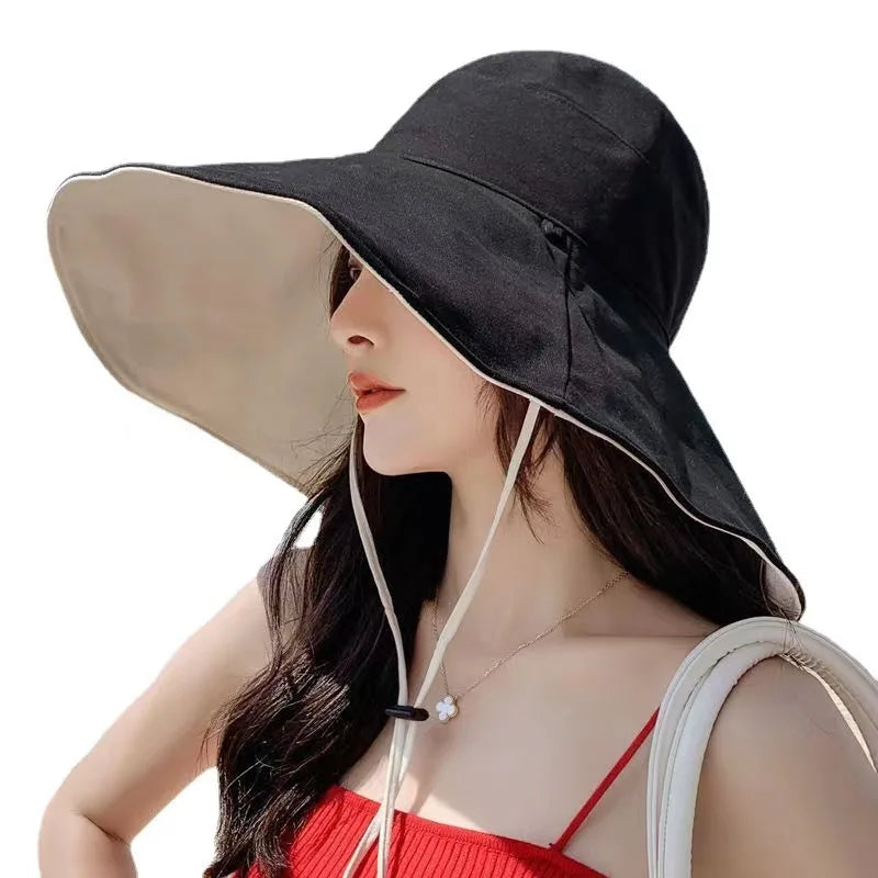 A woman wearing a Tidesmit reversible, black and beige wide-brim sun hat with an adjustable chin strap.