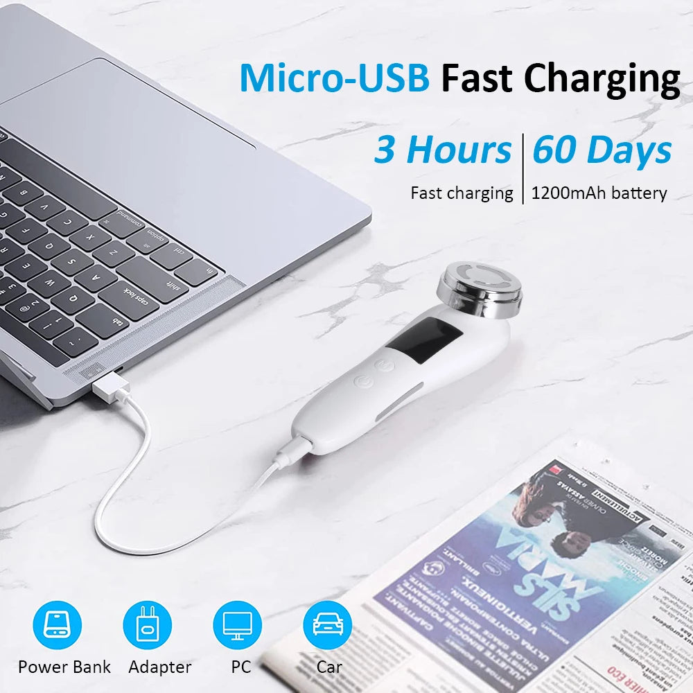White, handheld RF facial massager with a metallic head, charging via USB cable connected to a laptop.