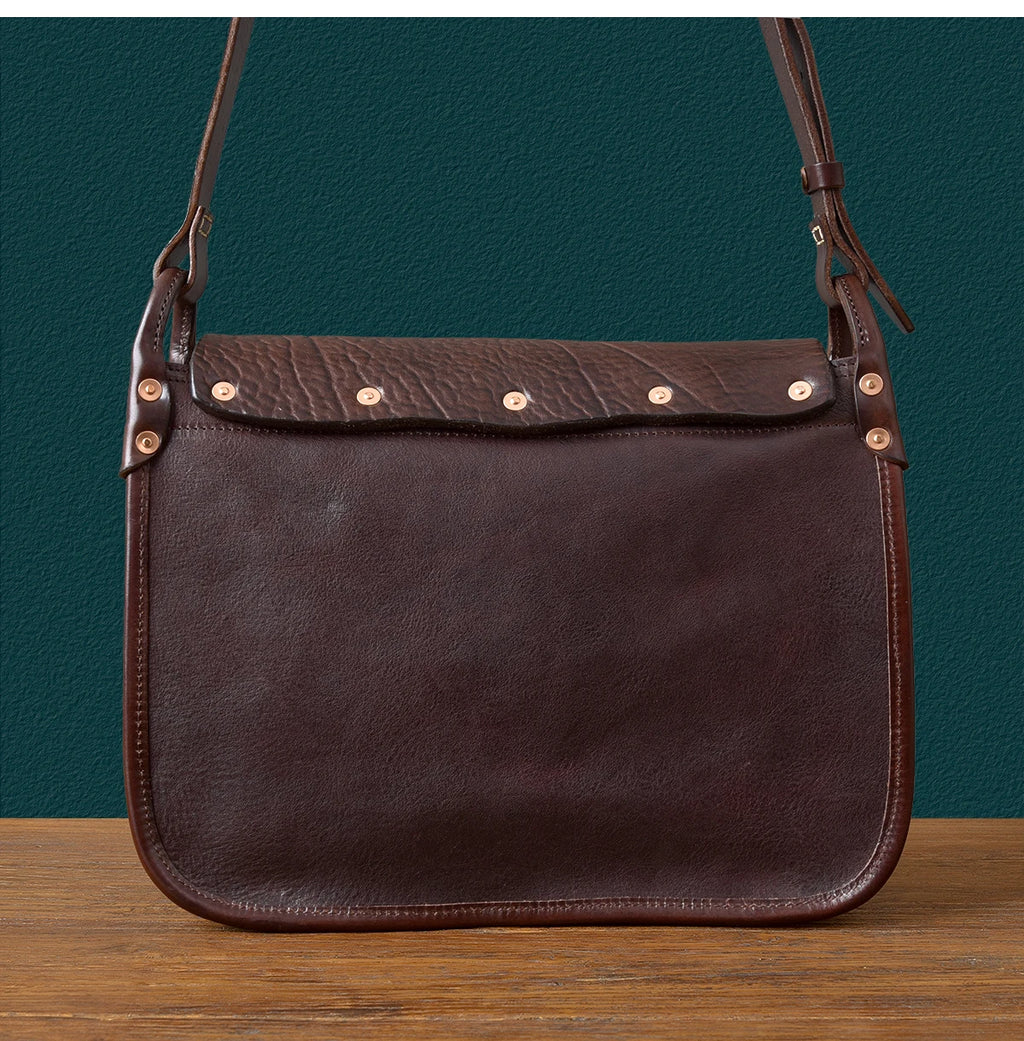Vintage handmade dark brown cowhide messenger bag with a textured flap, metal rivets, and adjustable shoulder strap.