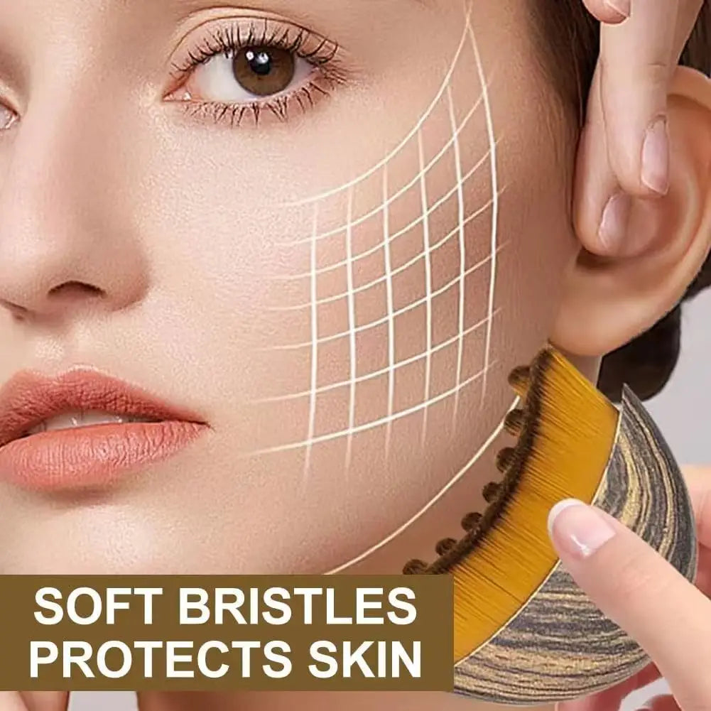 A contoured, oval facial massage brush with dense, golden-yellow bristles and a dark, wood-grain patterned handle.