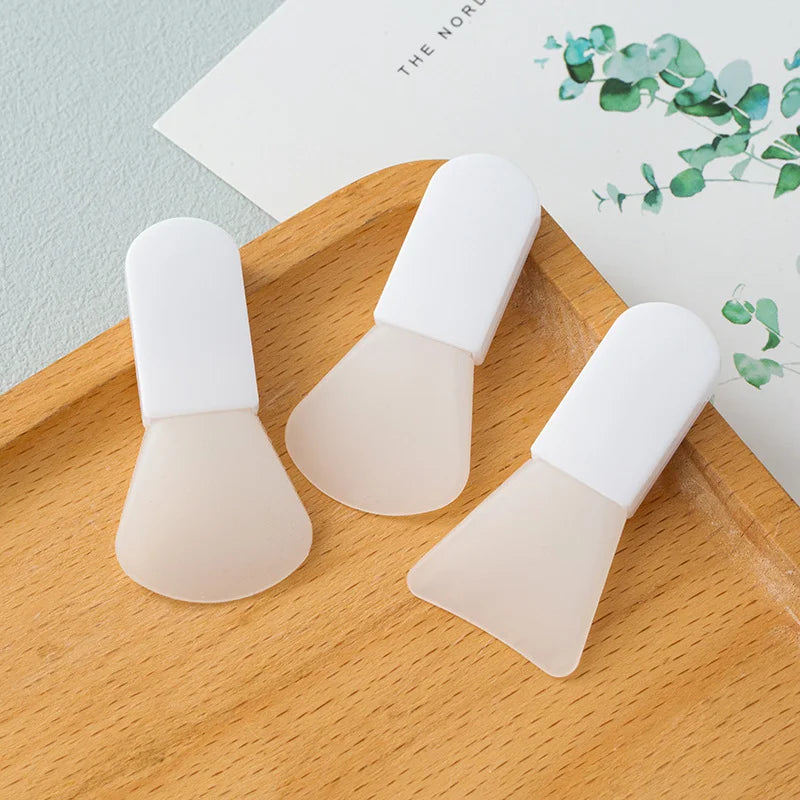 Three small, white-handled silicone facial mask spatulas with flexible, translucent fan-shaped applicator tips.