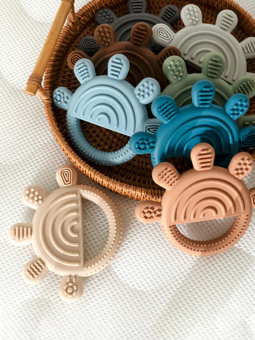 Colorful silicone baby teething rings in a woven basket. Assorted rainbow-shaped teething toys for infants.