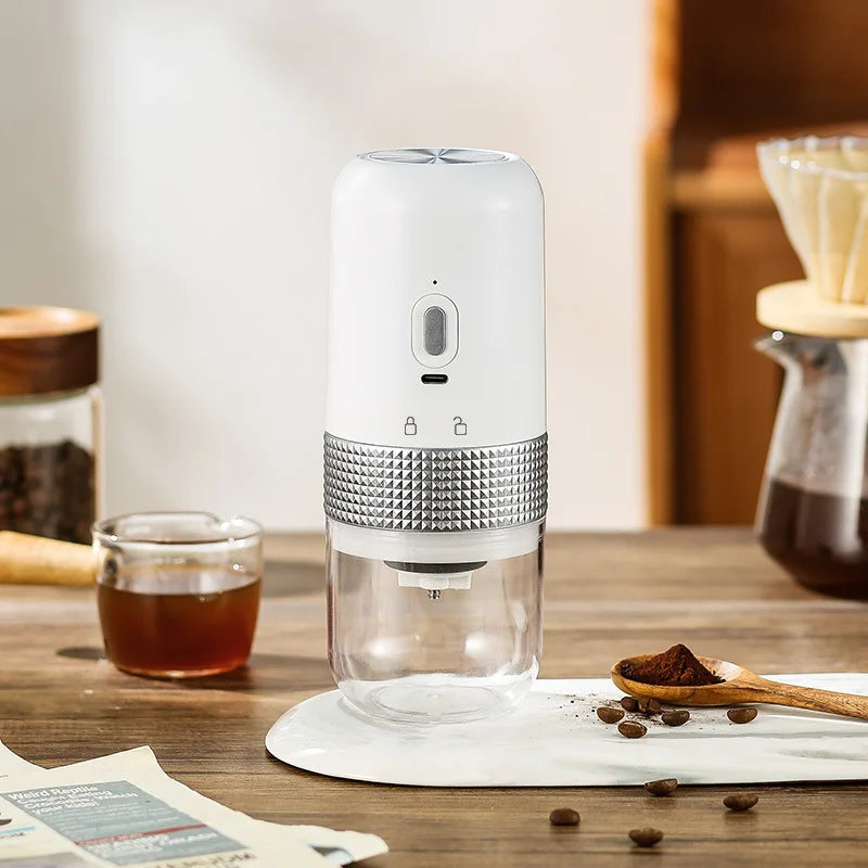 Portable white electric coffee bean grinder with silver textured grip and clear container on a wooden table.