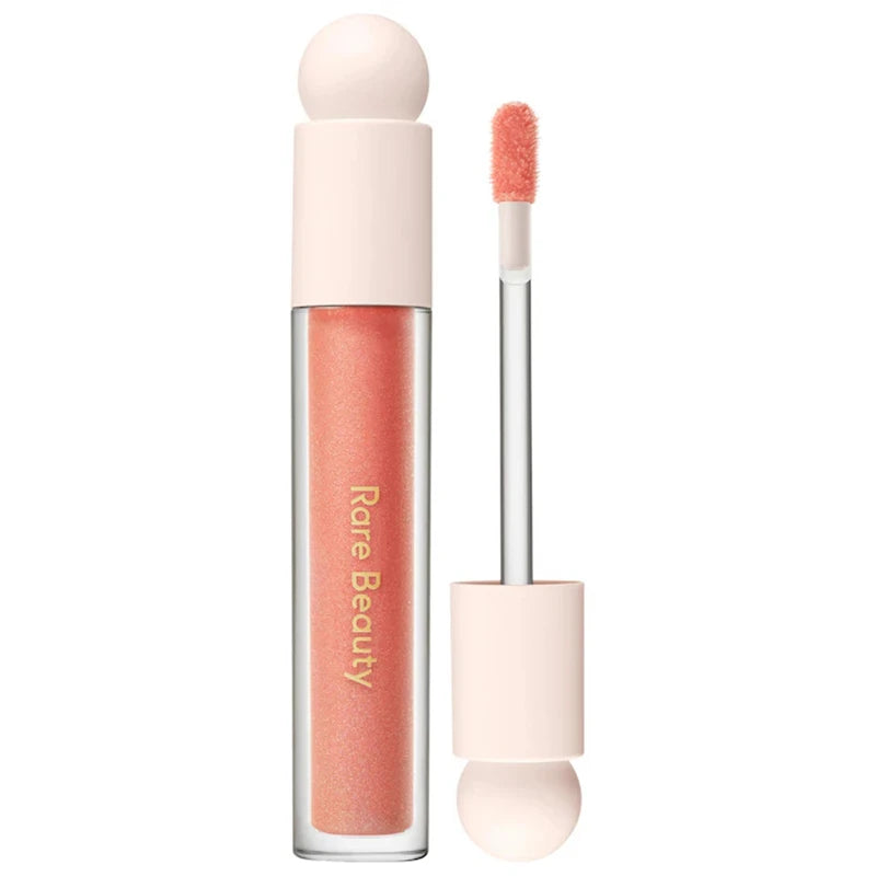 Rare Beauty Soft Pinch Tinted Lip Oil in a coral peach shade with a doe-foot applicator, creating a glossy stain finish.