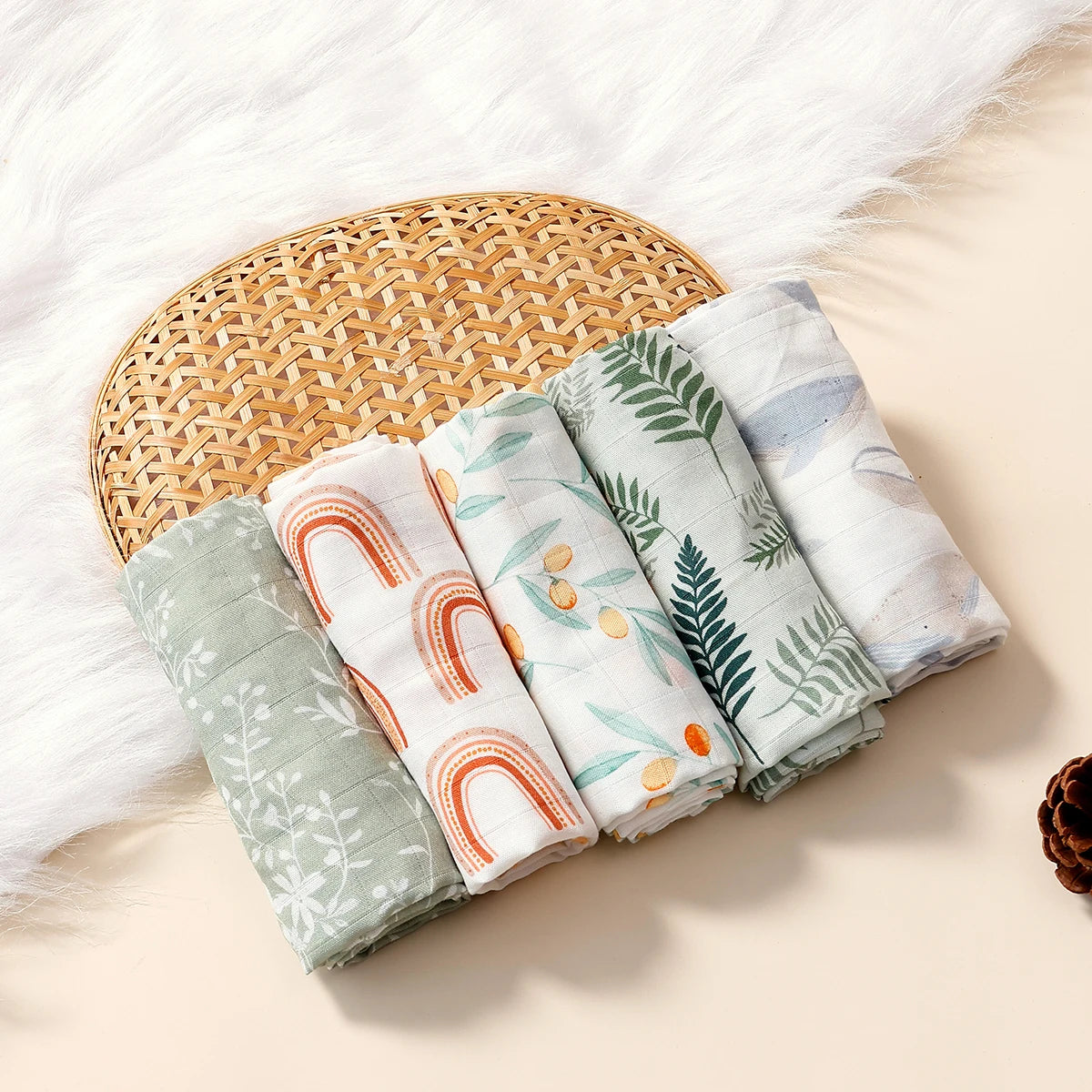 Set of 5 baby muslin swaddle blankets with rainbow, floral, and leaf prints on a woven basket. Soft baby care nursery.