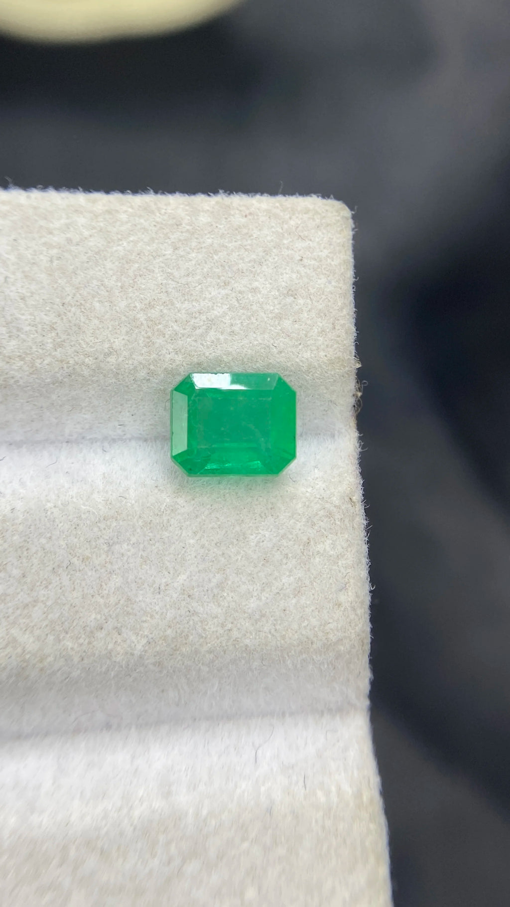 Loose green emerald-cut octagon emerald gemstone on white display pad