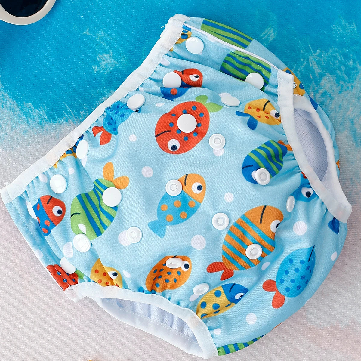Reusable cloth baby swim diaper with colorful fish print and adjustable snap buttons.