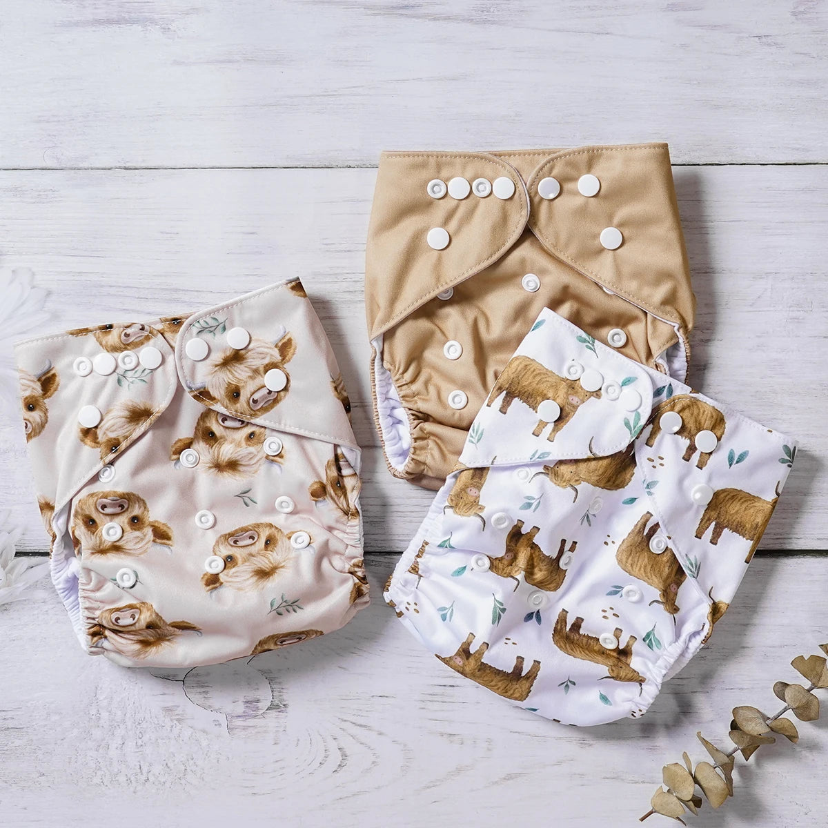 Set of 3 reusable baby cloth diapers with highland cow prints and solid tan, featuring adjustable snap buttons.