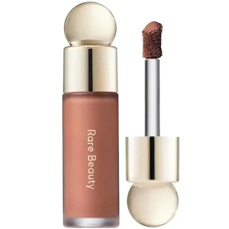 Rare Beauty liquid blush in a soft mauve shade with applicator wand, gold cap, and sleek frosted glass bottle.