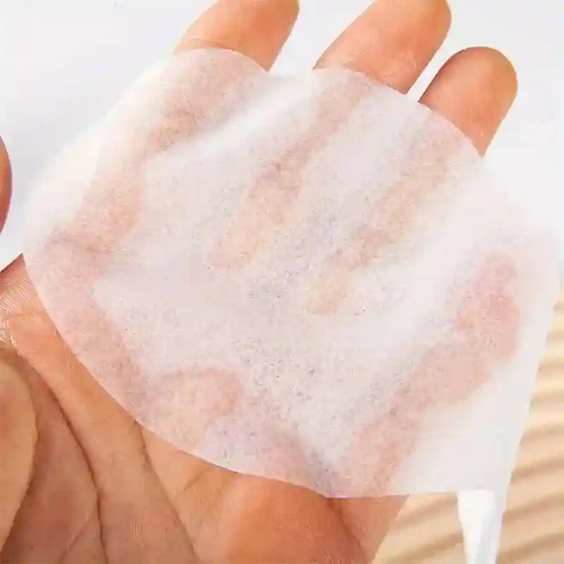 A hand holding a thin, white, circular disposable cotton eye mask sheet with a translucent, fibrous texture.
