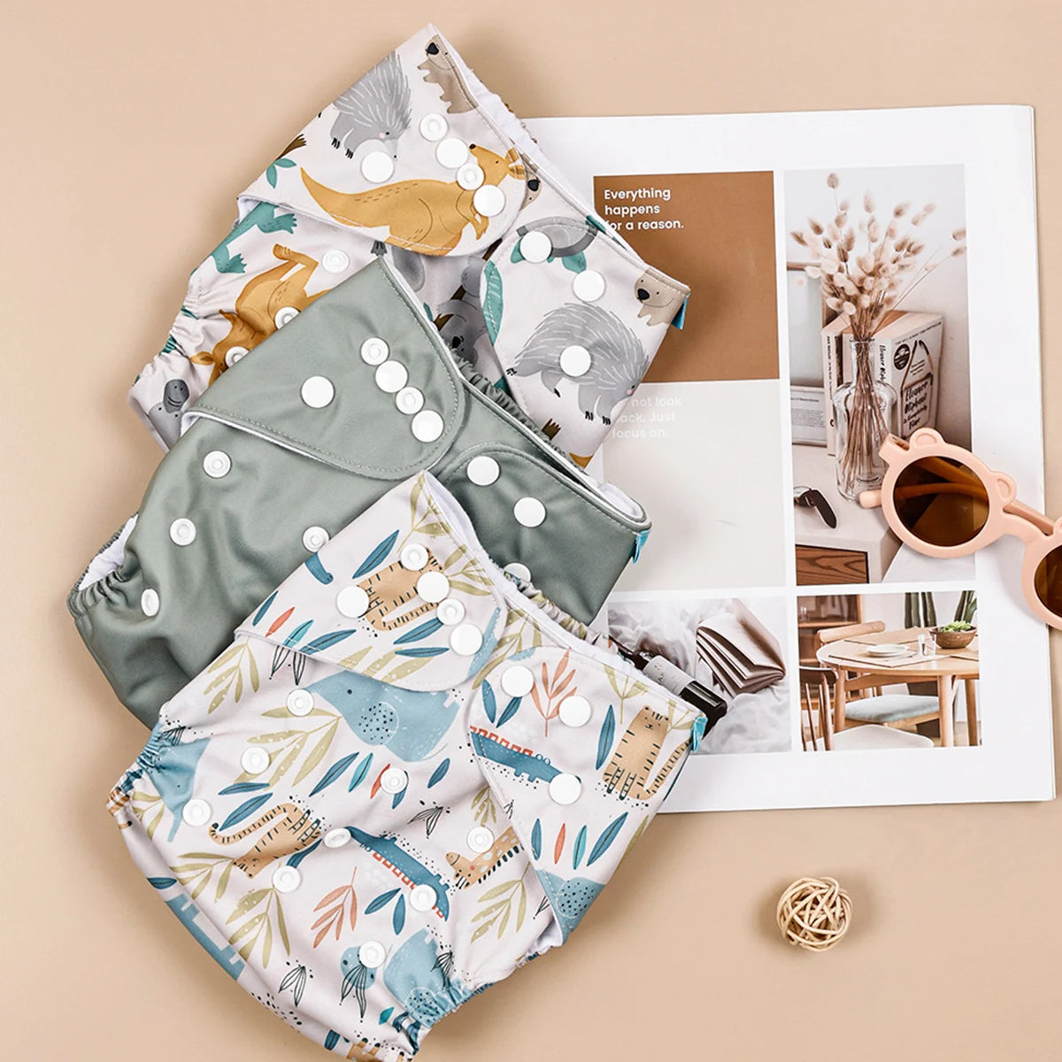 Reusable cloth baby diapers set with snap buttons, featuring dinosaur and animal prints in green and neutral tones.