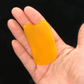 A hand holds a smooth, bright yellow resin gua sha facial massage tool with a curved, ergonomic shape.