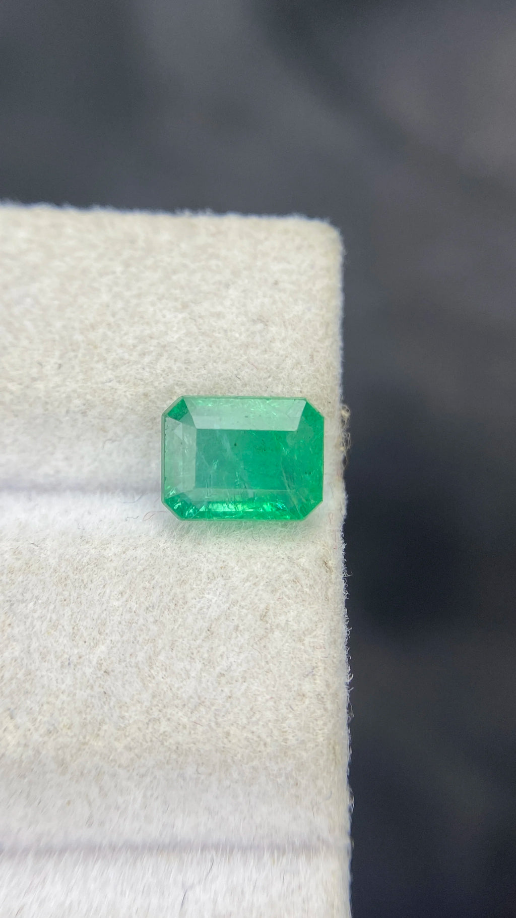 Green emerald-cut octagon gemstone on white cloth, angled view of facet edges