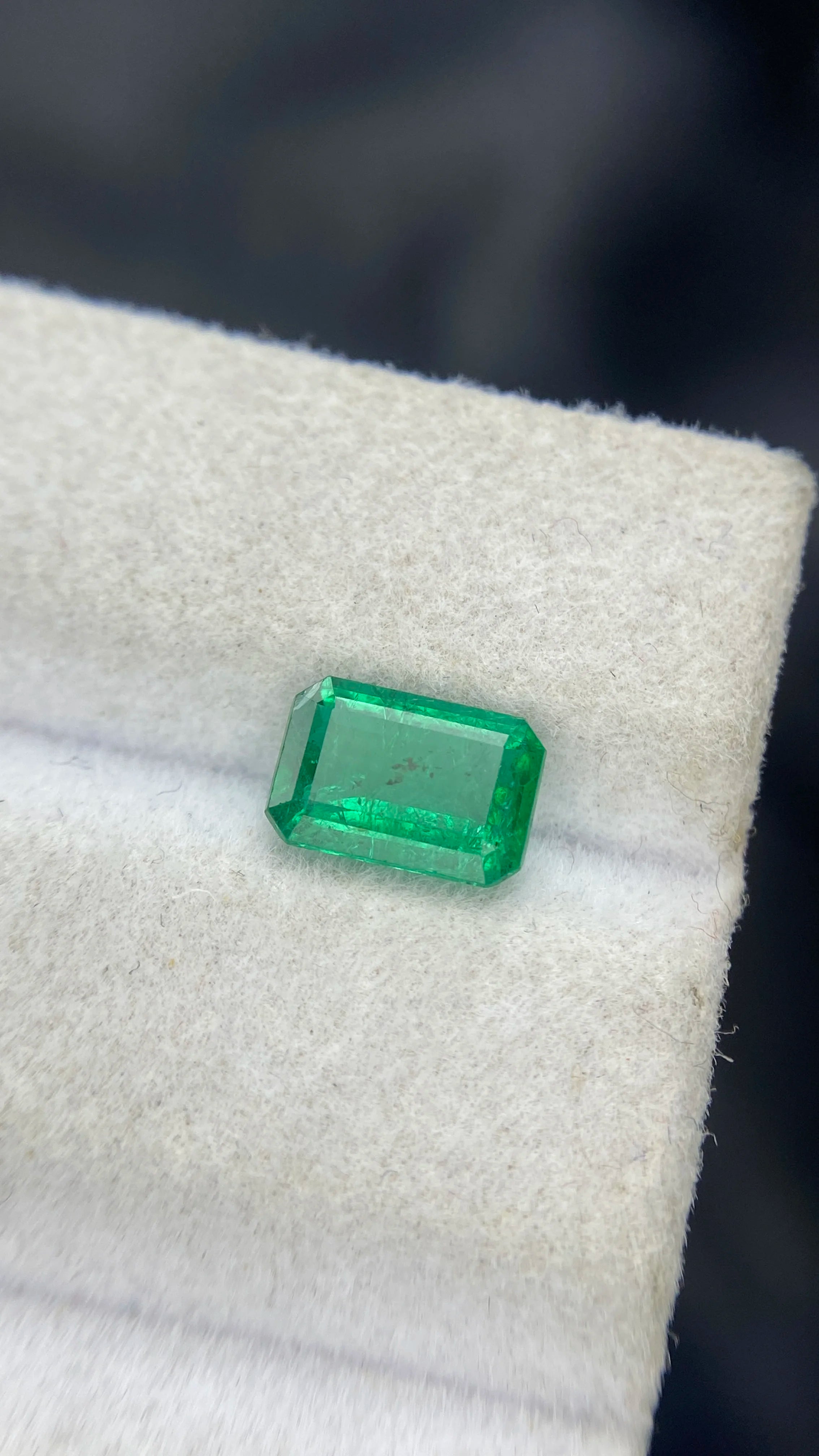 Small green emerald-cut gemstone on white display, loose stone for jewelry