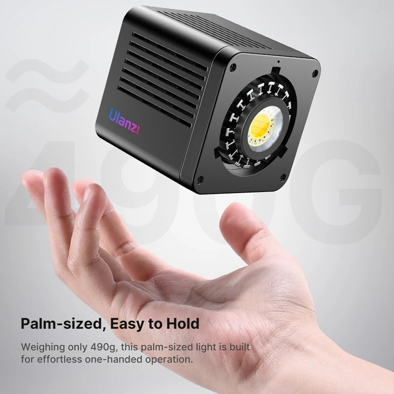 Compact black cube-shaped LED video light with side cooling vents, held in a hand for portable lighting.