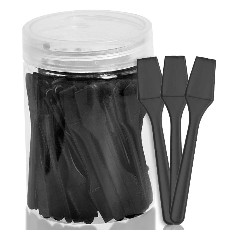 A clear plastic jar filled with black plastic mini cosmetic spatulas, with three individual scoops displayed in front.