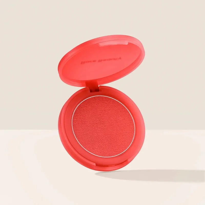 Rare Beauty compact powder blush in a vibrant coral-red shade with a smooth, soft-matte texture in a round case.