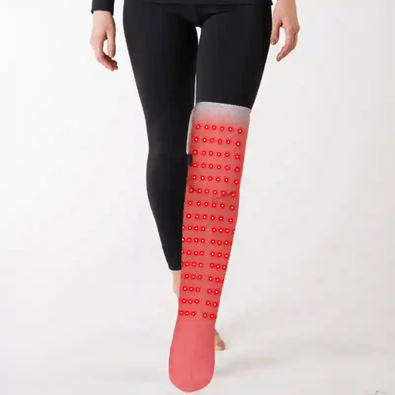 A person wearing a long, red fabric heating boot on one leg, featuring a grid of red LED therapy lights.