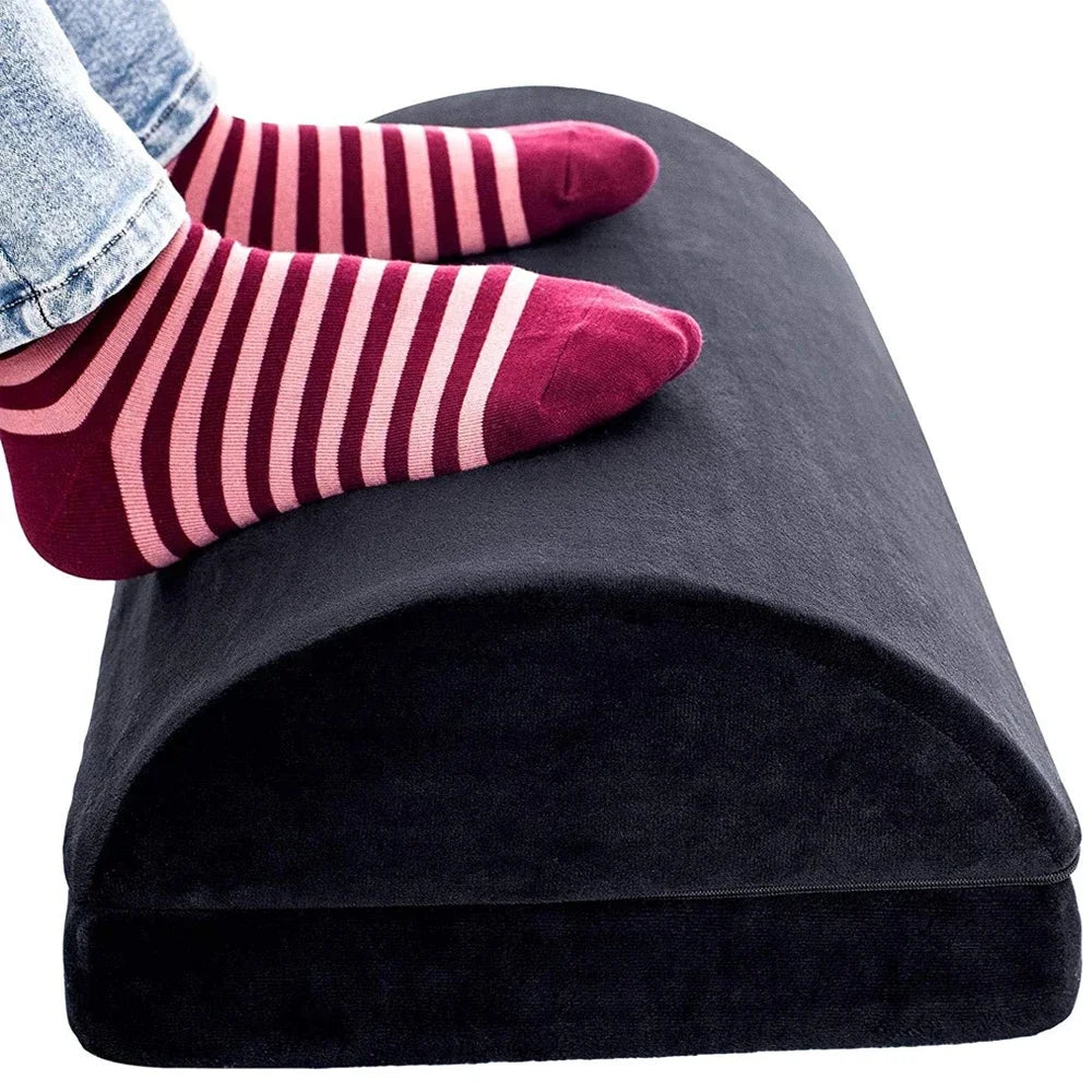 Black ergonomic under-desk footrest for back and knee pain relief, showing feet resting on the adjustable cushion.