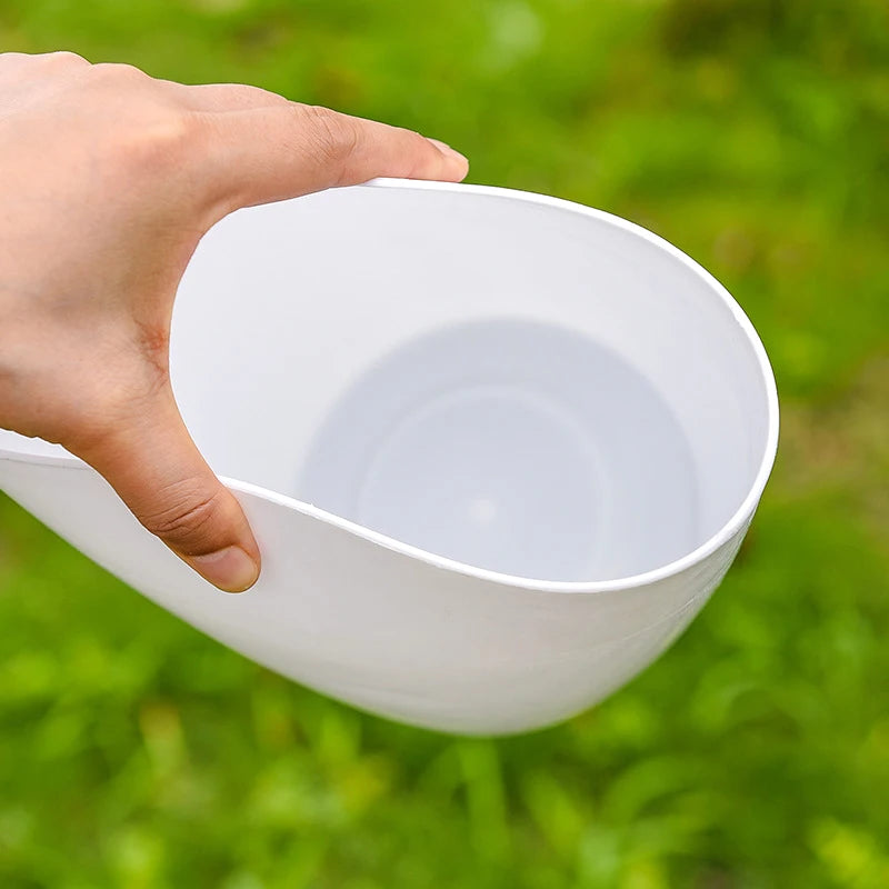 White self-watering plant pot with black rim held in one hand.
