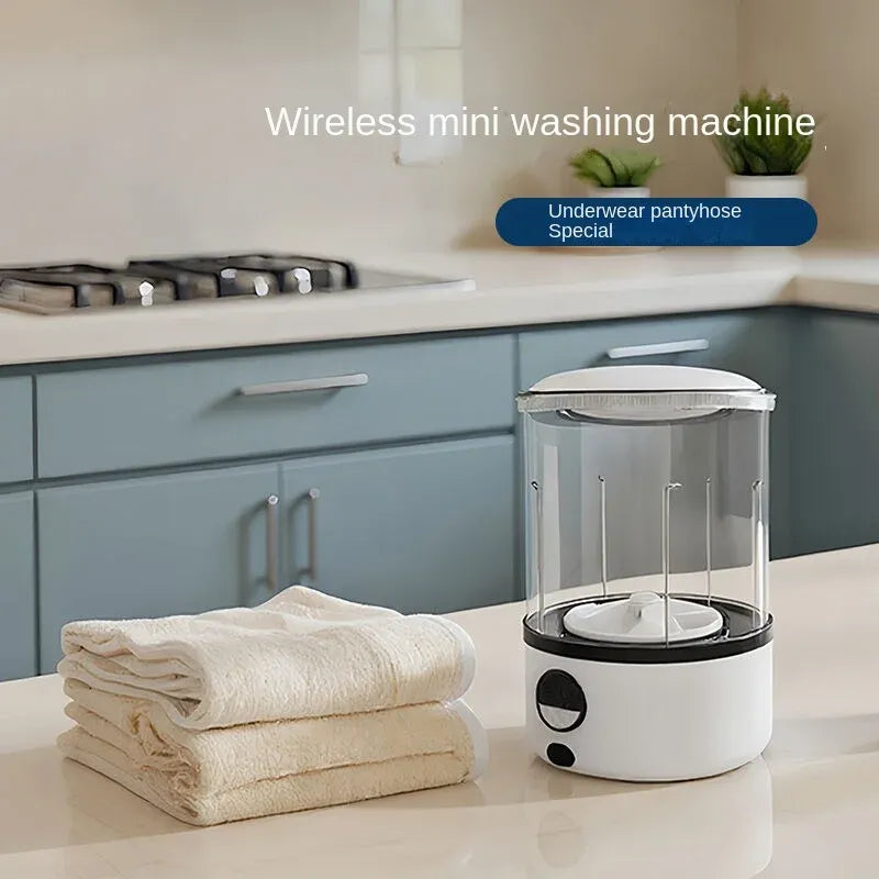 Wireless mini washing machine for underwear and delicate garments on a countertop beside folded towels.