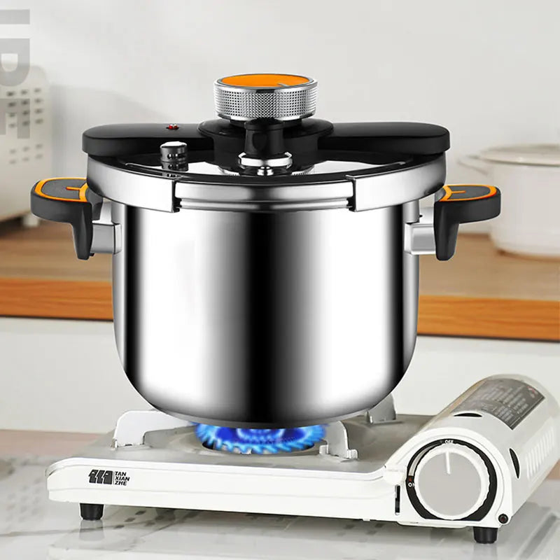 Stainless steel pressure cooker on cooktop, with black lid and orange steam vent cap