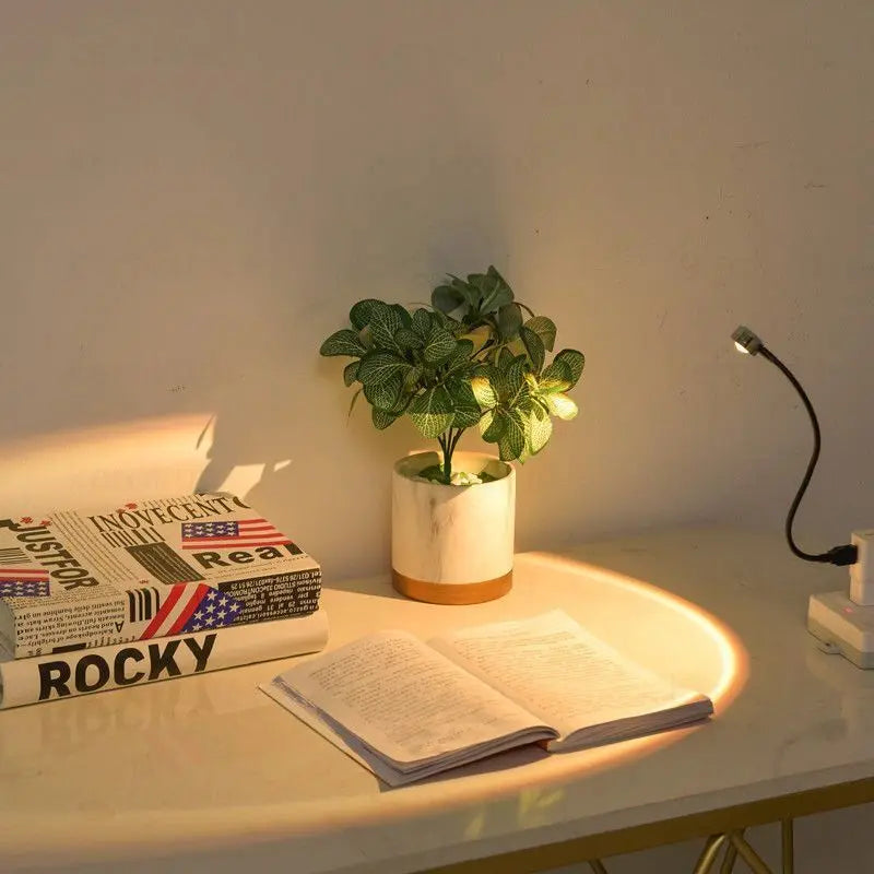 Sunset projection lamp with a flexible neck, sitting on a white desk next to a marble plant pot and open books.