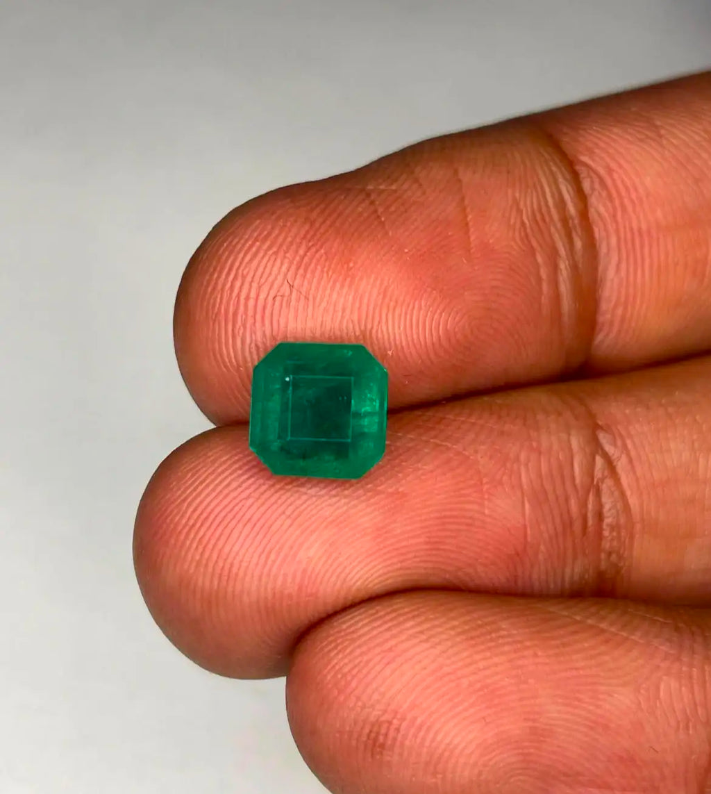 Green emerald gemstone, square octagon cut held in fingertips, front view