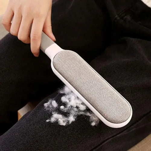 Grey plush pet hair removal brush gliding over dark sofa fabric with lifted lint
