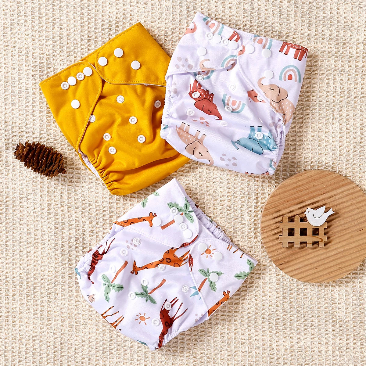 Reusable cloth diapers in yellow and prints featuring elephants, giraffes, and rainbows. Adjustable baby diaper set.