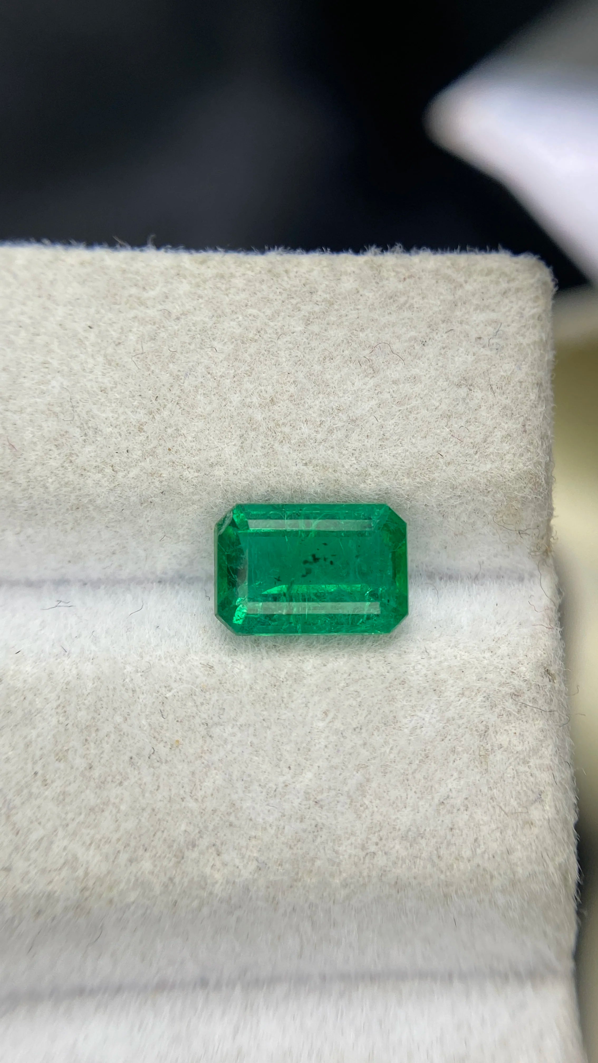 Green emerald-cut gemstone with long rectangular shape, loose stone on white padding