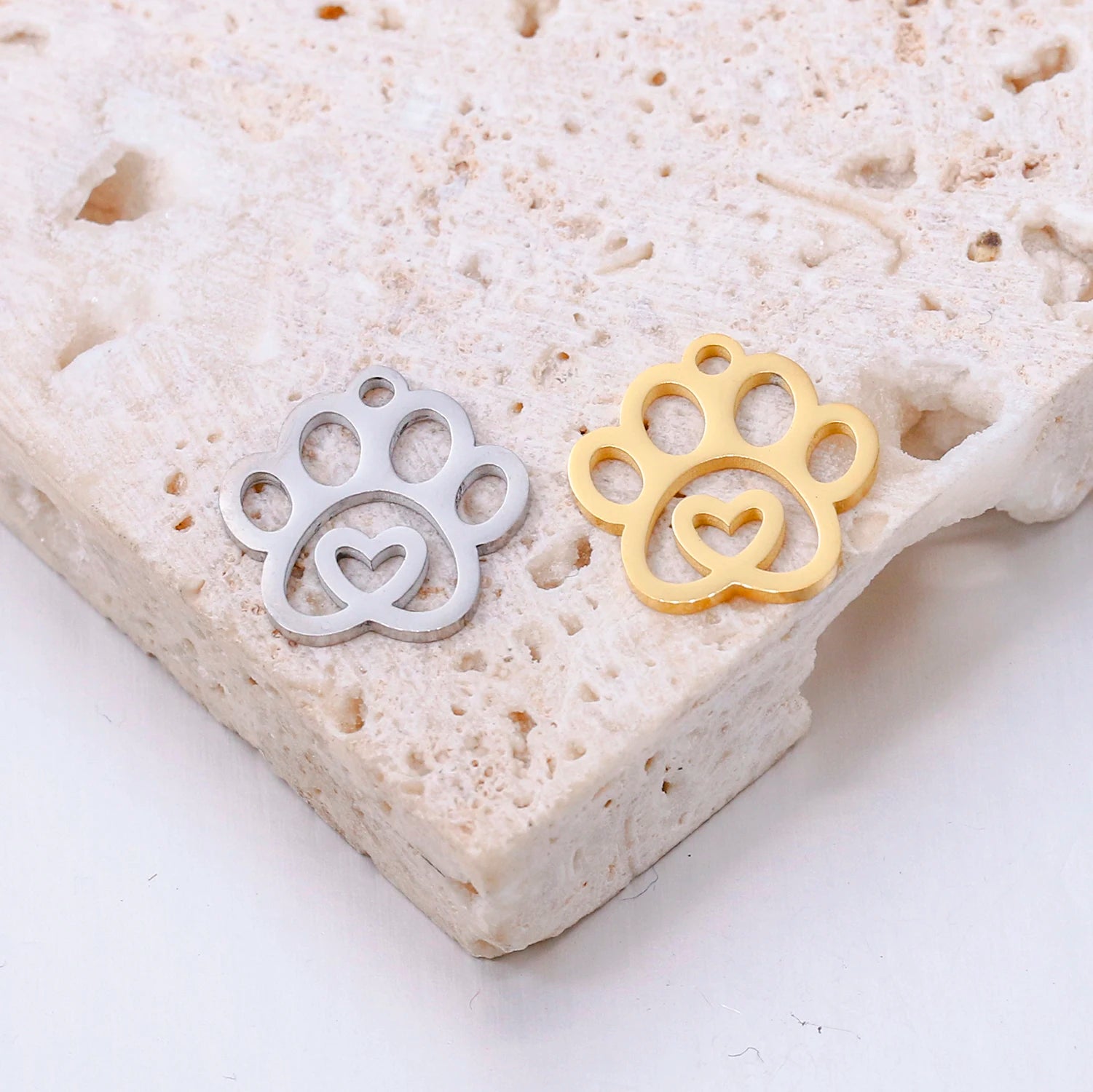 Gold and silver stainless steel dog paw print charms with heart cutouts for DIY pet jewelry and necklace making.