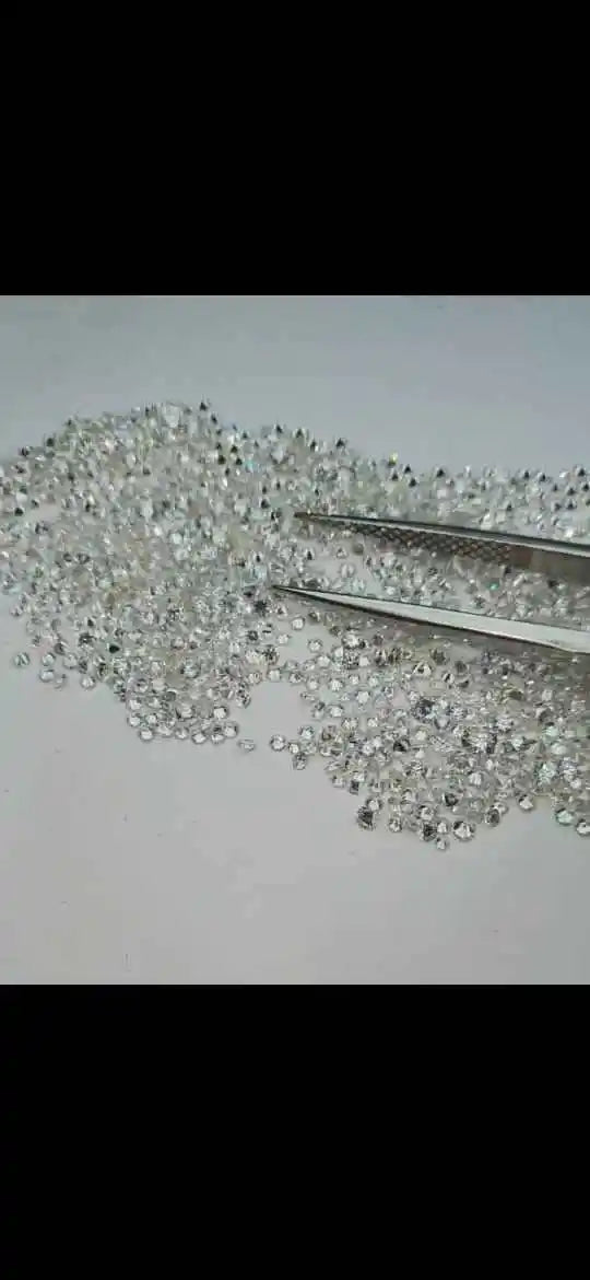 Loose lab-grown round brilliant diamond stones on surface, metal tweezers beside stones