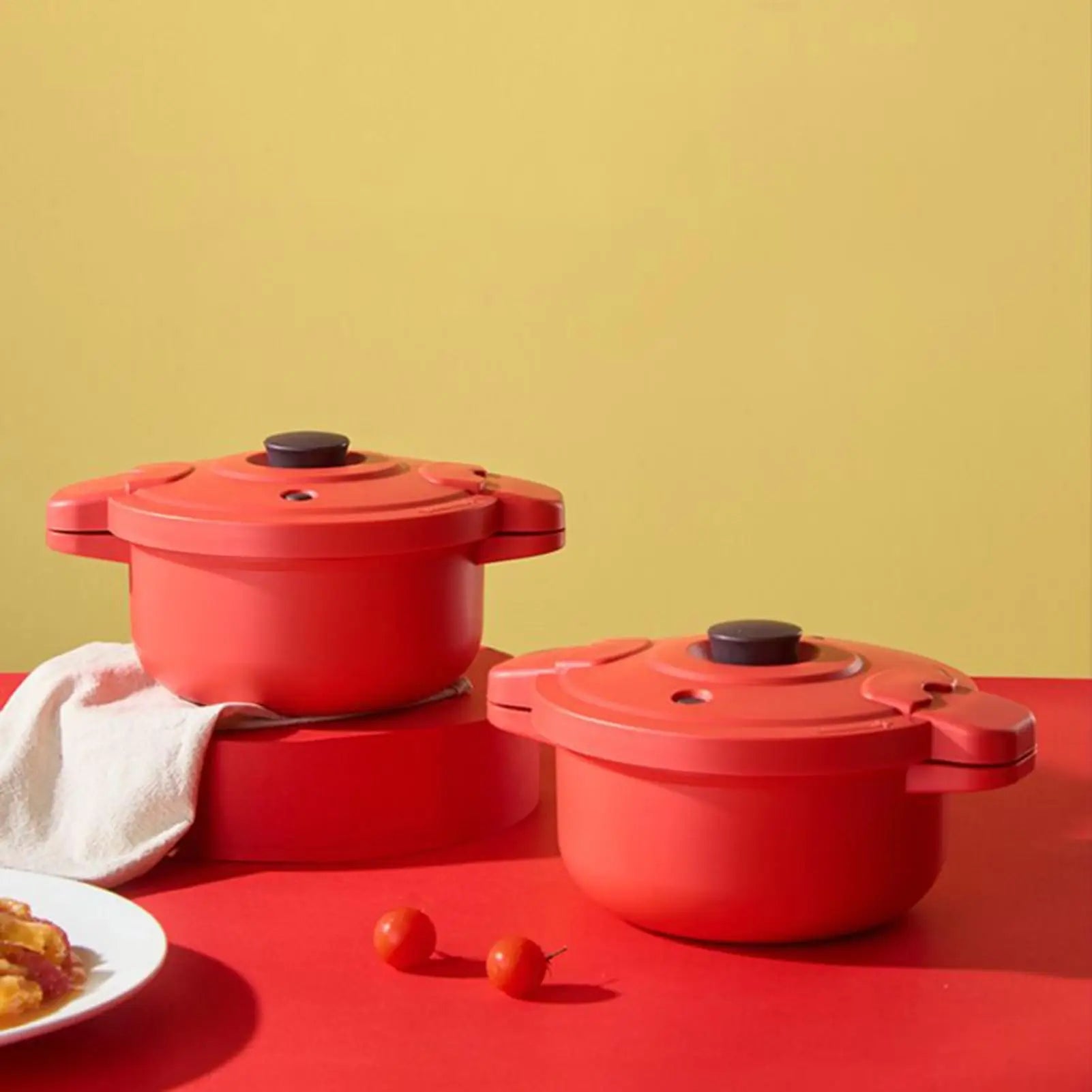 Two red pressure cooker pots with black knobs stacked on counter.