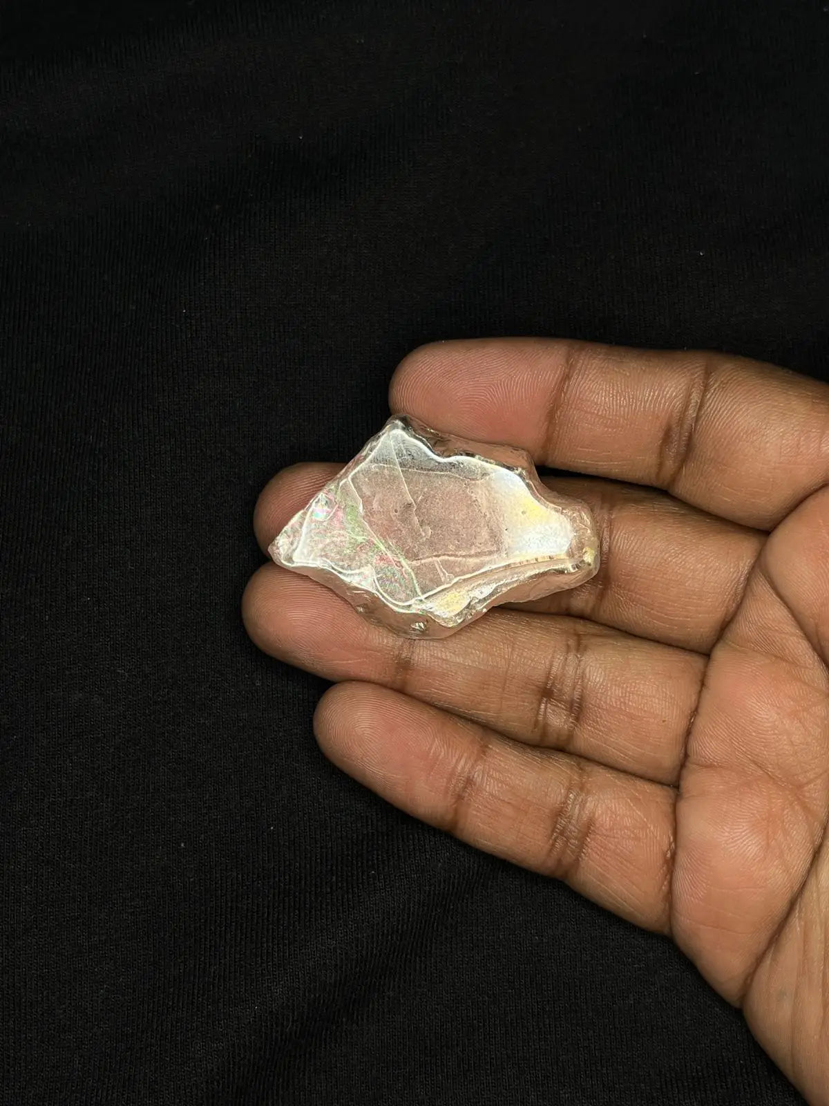 Hand holding iridescent rough gemstone, flat faceted piece with rainbow color flash