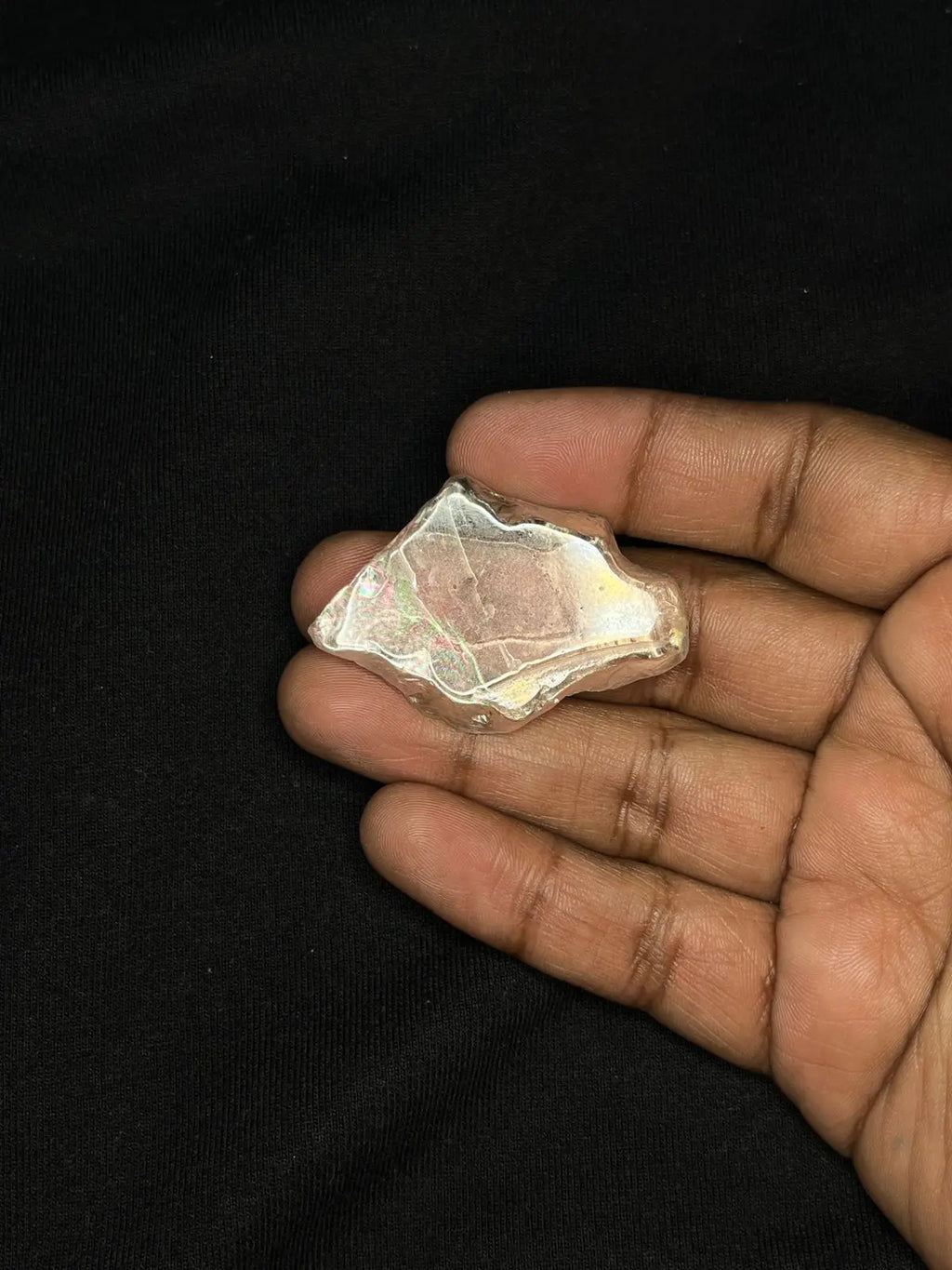 Hand holding iridescent rough gemstone, white-toned piece with soft rainbow shimmer