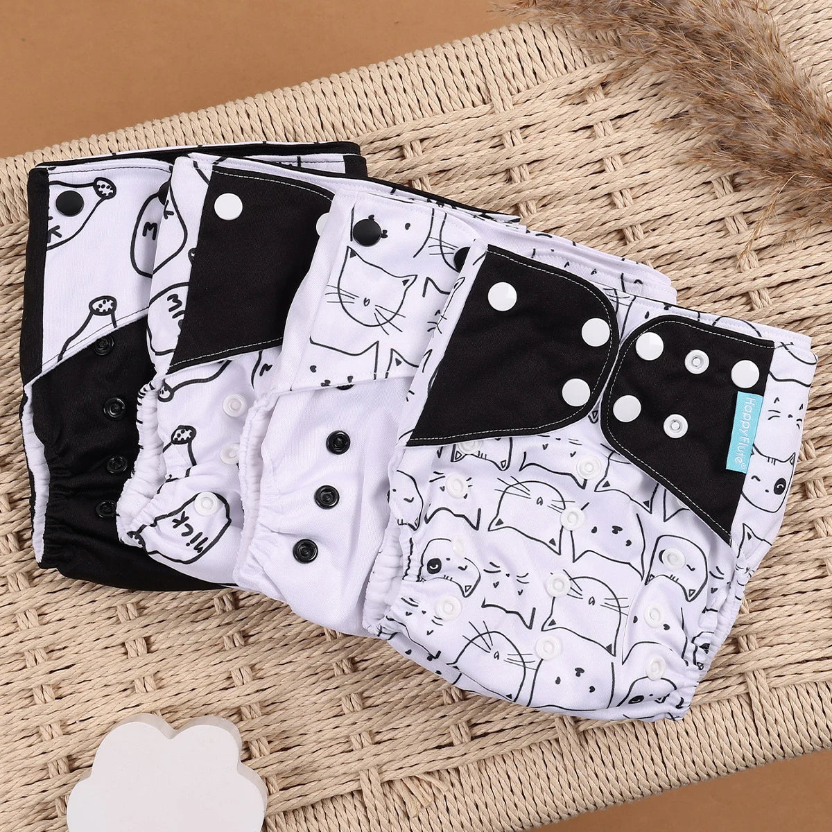 Happy Flute reusable cloth baby diapers with black and white cat pattern on a wicker background.